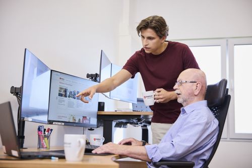 Zwei Malteser Kollegen sitzen vor Computerbildschirmen und sprechen über eine digitale Fortbildung.