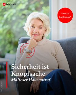 Eine ältere Frau im braunen Pullover und dunkelblaufer Hose sitzt und lächelt in die Kamera. Am rechten Handgelenk hat sie den Haunsotrufknopf um.