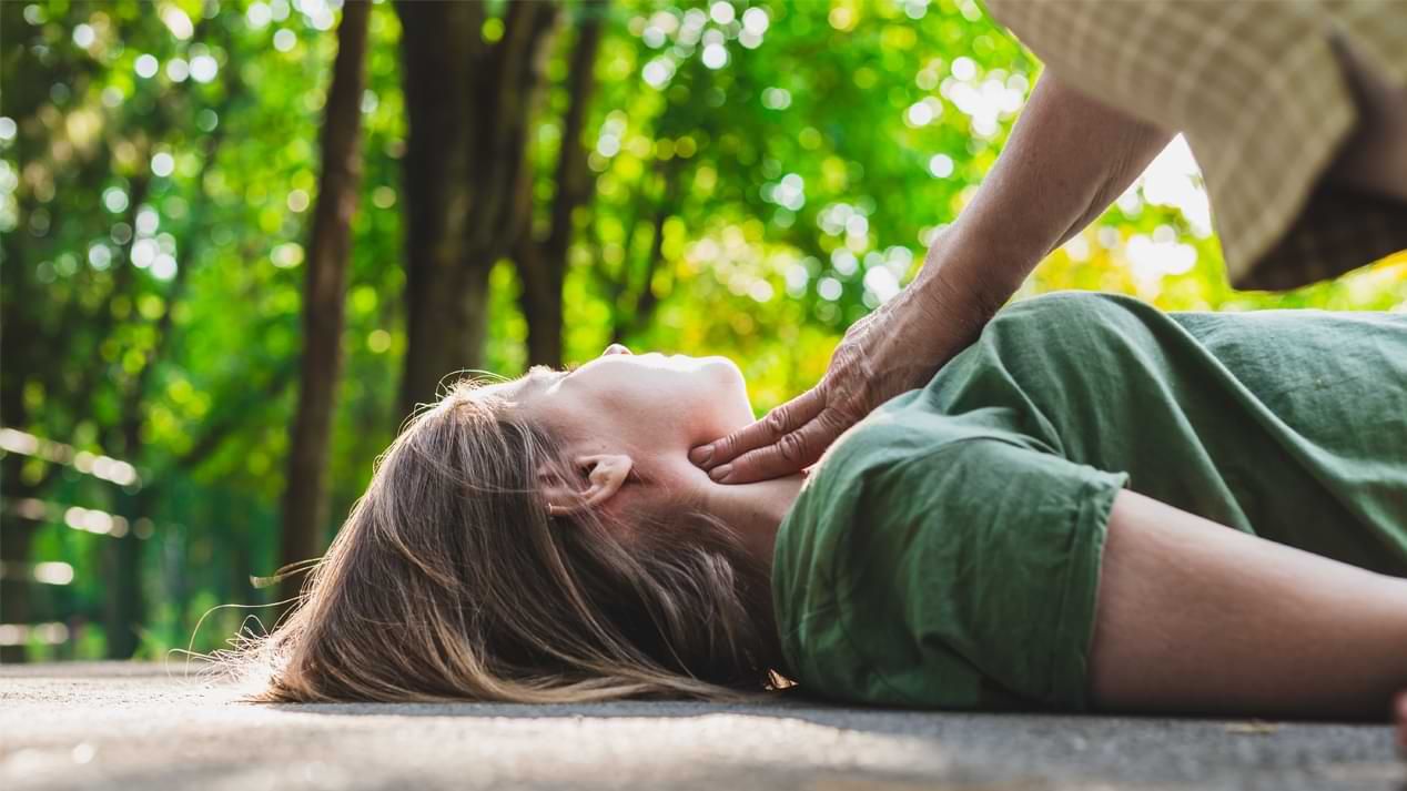 Eine ältere Frau überprüft den Puls eines jüngeren, bewusstlosen Mädchens.