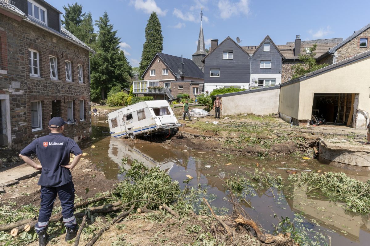 Ein Junger Mann mit in die Hüften gestemmten Armen schaut auf eine von Hochwasser zerstörter Straße.