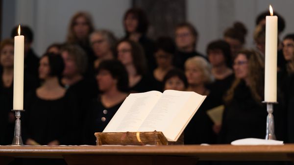 Ein aufgeschlagenes Buch zwischen zwei Kerzen, dahinter eine Gruppe stehender Menschen