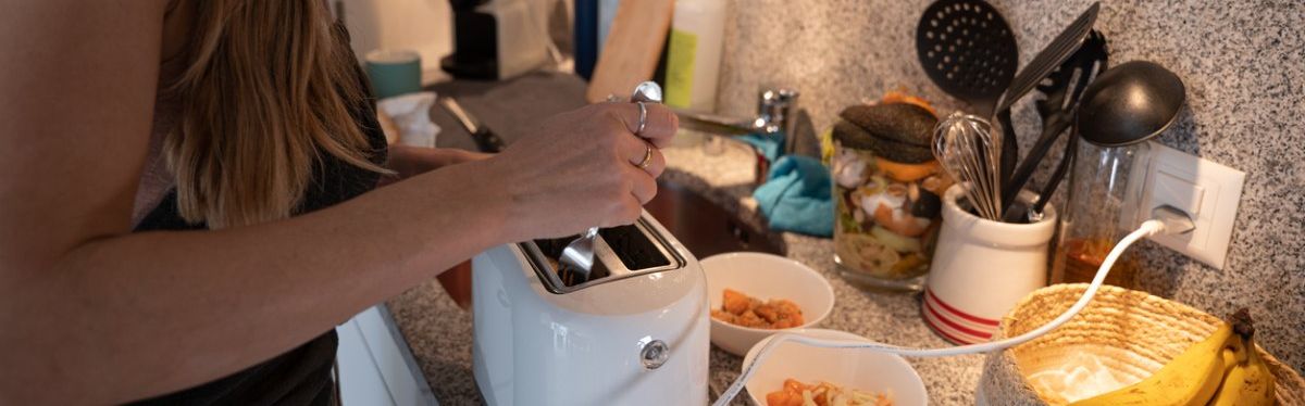 Eine junge Frau stochert mit einer Gabel in einem Toaster herum.