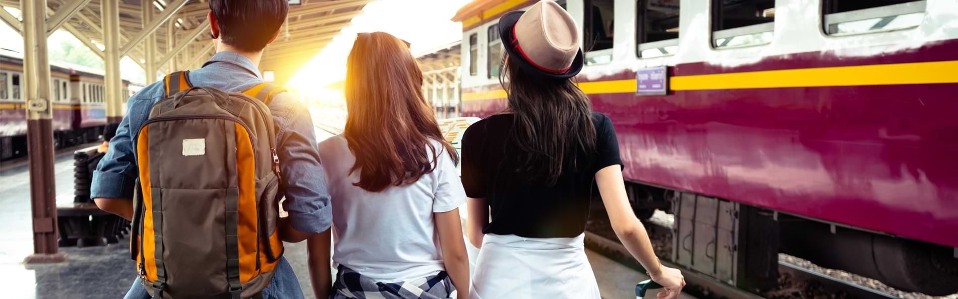 Drei Personen stehen mit ihrem Reisegepäck an einem Bahnhof.