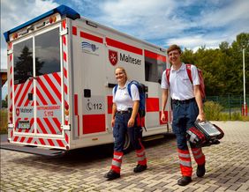 Zwei junge Sanitäter mit Notfallrucksäcken haben den Rettungswagen verlassen und sind bereit für den Einsatz.