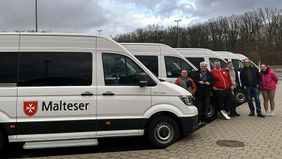 Sechs Männer und Frauen stehen neben mehreren Malteser Behindertentransportfahrzeugen.