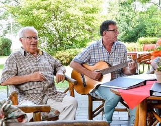 Zwei Männer sitzen im Garten, einer spielt Gitarre