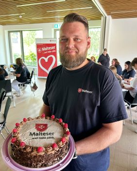 Mann mit einer selbstgebackenen Torte mit Malteser Logo.