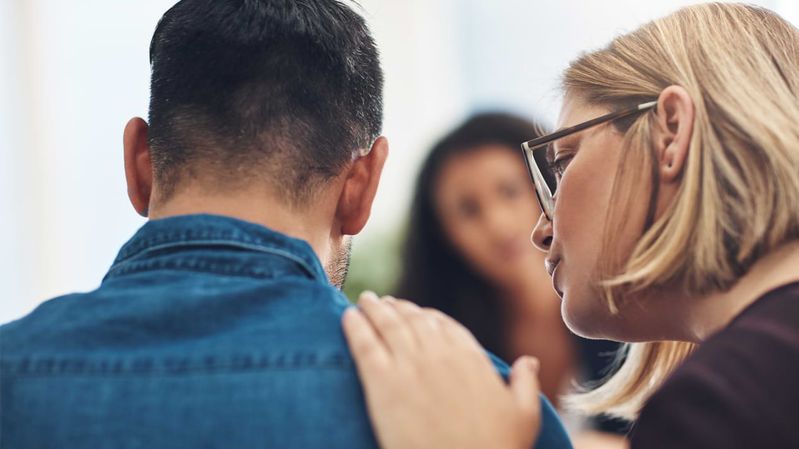 Eine Frau legt einem Mann die Hand tröstend auf die Schulter