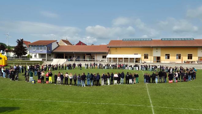 Viele junge Menschen stehen in einem großen Kreis auf einem Sportplatz.