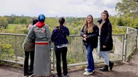 Mehrere Frauen stehen an einer Brüstung und schauen über eine grüne Landschaft.