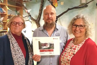 Zwei Frauen und ein Mann halten einen Scheck.