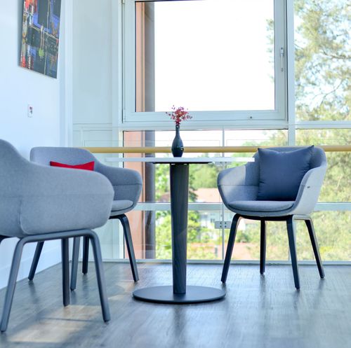 Sitzecke im Wintergarten mit drei Sesseln, kleinem Tisch und großer Fensterfront.