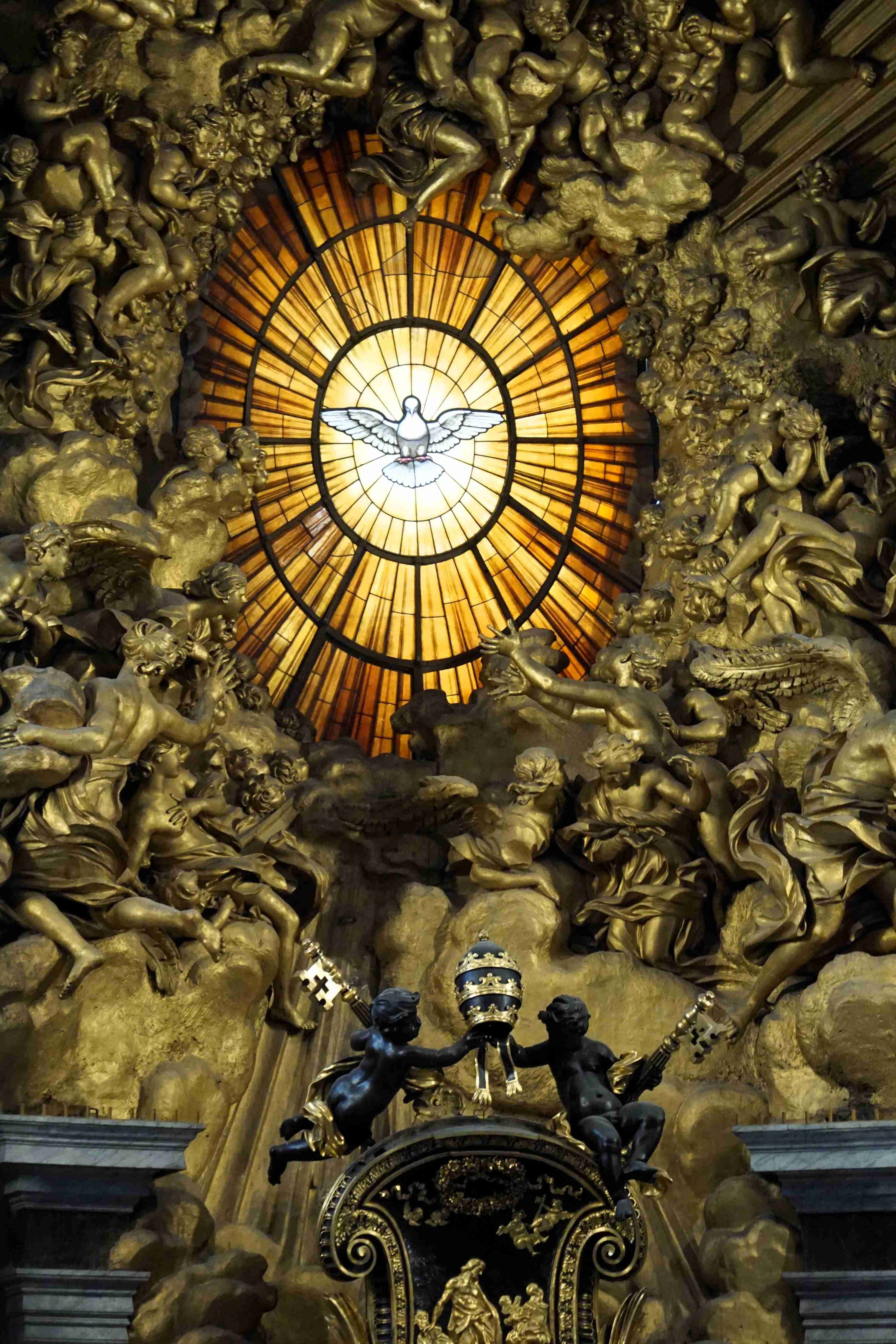 Goldene Verzierung mit strahlenförmigem Muster und Taube im Zentrum, umgeben von barocken Verzierungen.