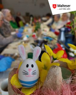 Im Vordergrund ist ein bemaltest Osterei und im Hintergrund die Seniorinnen und Senioren beim Verzieren der Eier.