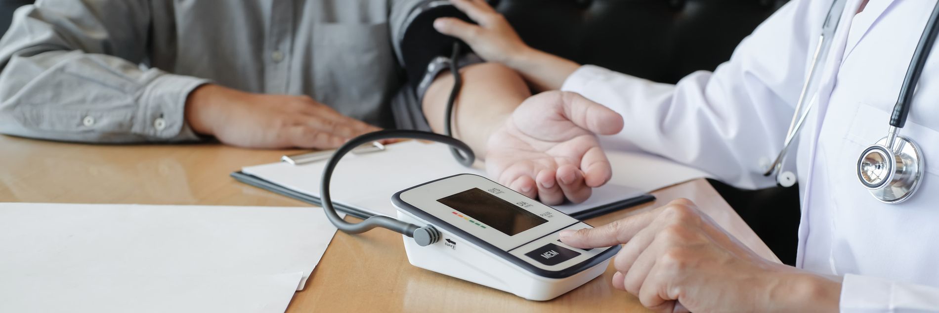 Ärztliche Fachkraft misst bei einer Person den Blutdruck mit digitalem Messgerät und Manschette am Oberarm.