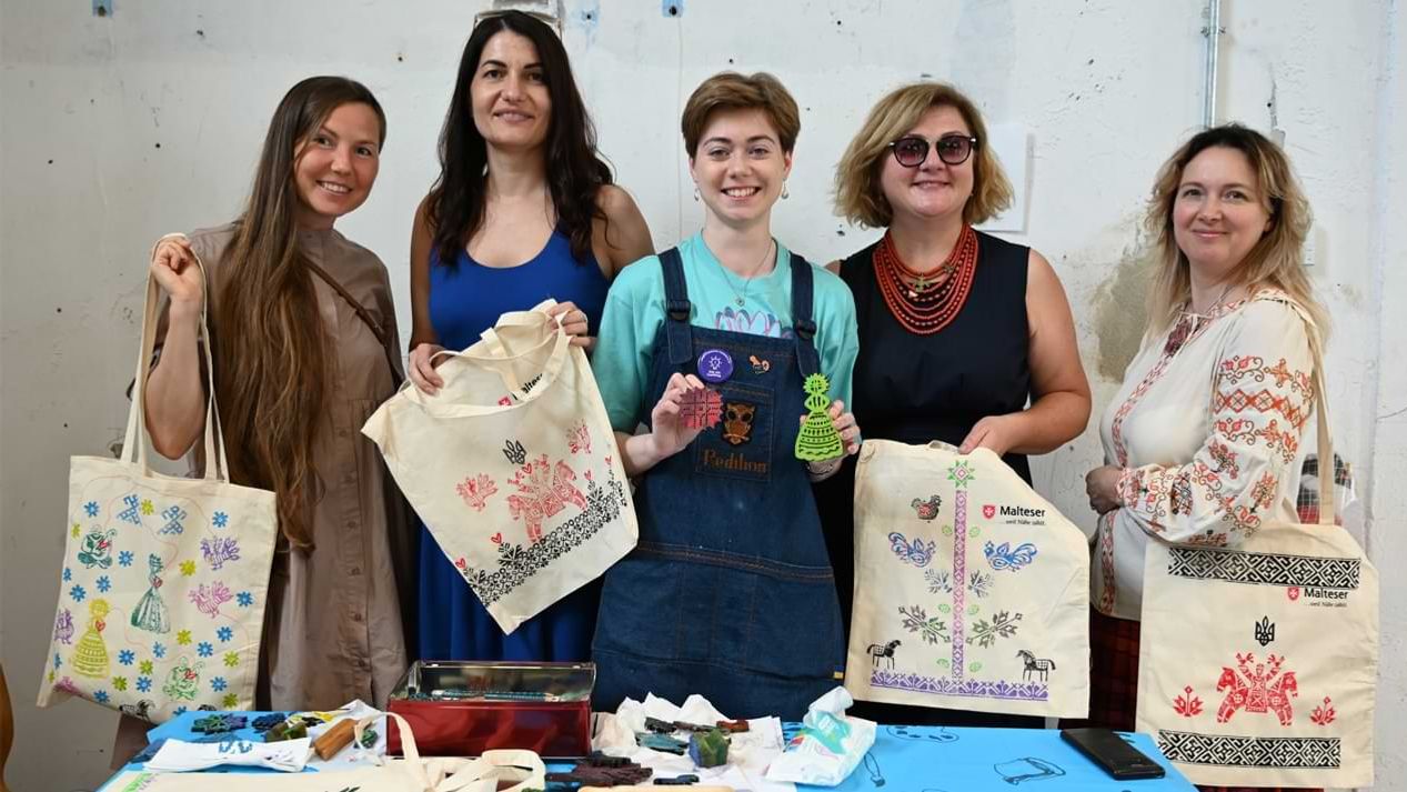 Eine Gruppe lächelnder Frauen mit kunstvoll gestalteten Jutetaschen.