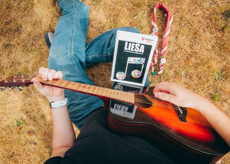 Junger Mann spielt sitzend Gitarre, ein Liederbuch liegt vor ihm.