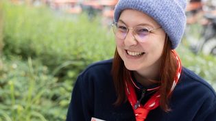 Junge Frau in Malteser Kleidung mit einer grauen Mütze sitzt im Freien an einer Schreibmaschine