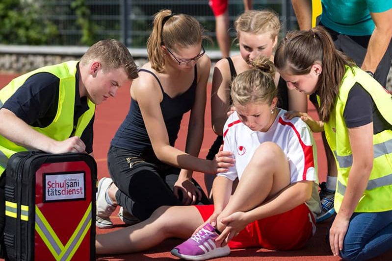 Malteser Schulsanitäter versorgen ein Mädchen, das sich beim Sport verletzt hat.