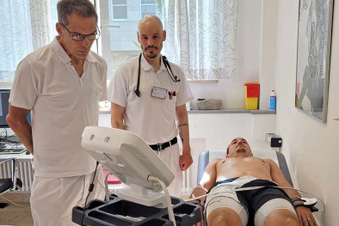 Zwei Ärzte überwachen eine Untersuchung bei einem Patienten, der mit Sensoren auf einer Liege liegt.