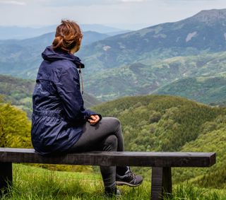 Eine Frau sitzt auf einer Bank und schaut in die weit entfernten Berge.