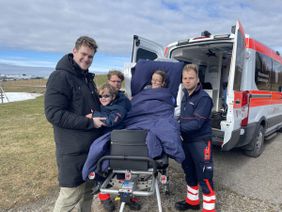 Auf dem Foto zu sehen sind Frau D. auf einer Liege, ihr Sohn und ihr Enkel sowie Thomas und Daniel vom Herzenswunsch-Team vor der wunderschönen Kulisse des Allgäus.