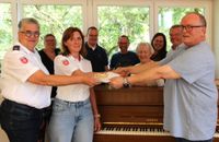 Zwei Vertreterinnen der Malteser nehmen vom Vorsitzenden des Chors die Spende entgegen. Im Hintergrund hat sich der Chor aufgestellt.