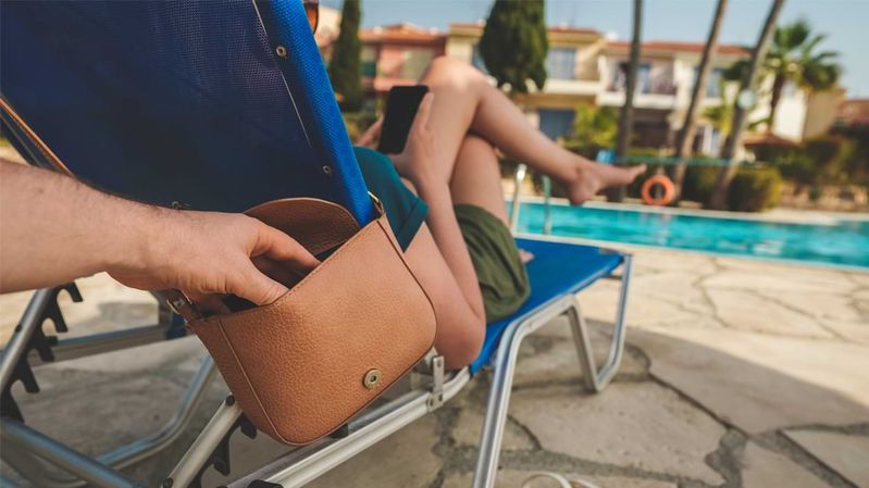 Am Rande eines Pools greift eine Hand in eine fremde Handtasche.