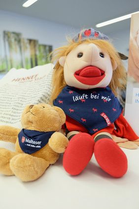 Das beliebte Begrüßungspaket für Neugeborene in Hennef wird durch ein weiteres kleines Willkommensgeschenk erweitert: Einen „Sabbellappe Hennes“ mit der Aufschrift "Läuft bei mir" hier getestet an Handpuppe Malte. 