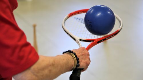 Person balanciert einen Ball auf einem Tennisschläger als Teil einer motorischen Übung.