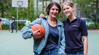 Eine junge Frau im Malteser Shirt mit einem Mädchen auf dem Basketballfeld. 