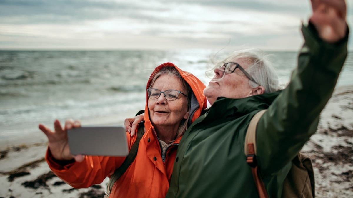 Zwei ältere Damen machen einen Strandspaziergang und fotografieren sich.