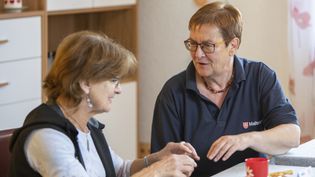 Frau mit Malteser Poloshirt und eine Seniorin an einem Tisch
