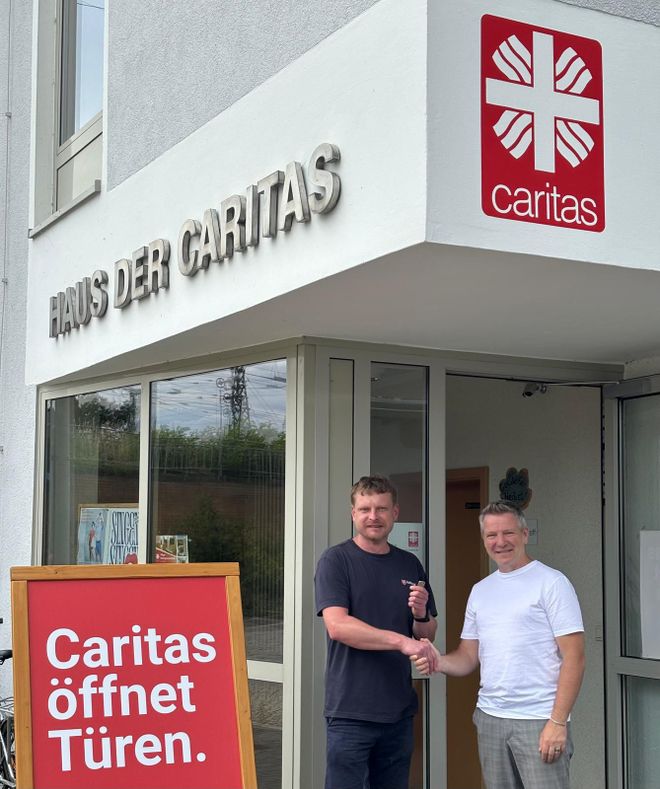 zwei Männer stehen vor dem Eingang der Caritas in Cottbus. Sie schütteln sich die Hände.