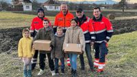 Vier Männer in Malteserkleidung stehen hinter vier Kindern und Jugendlichen, von denen zwei ein Hilfspaket in der Hand halten.
