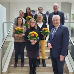 Gruppenfoto auf einer Treppe mehrere Personen halten Blumensträuße ein Mann steht vorn im Anzug.