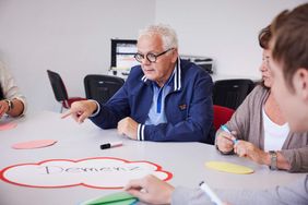 Älterer Mann zeigt in einer Besprechung auf eine Karte mit dem Wort „Demenz“.