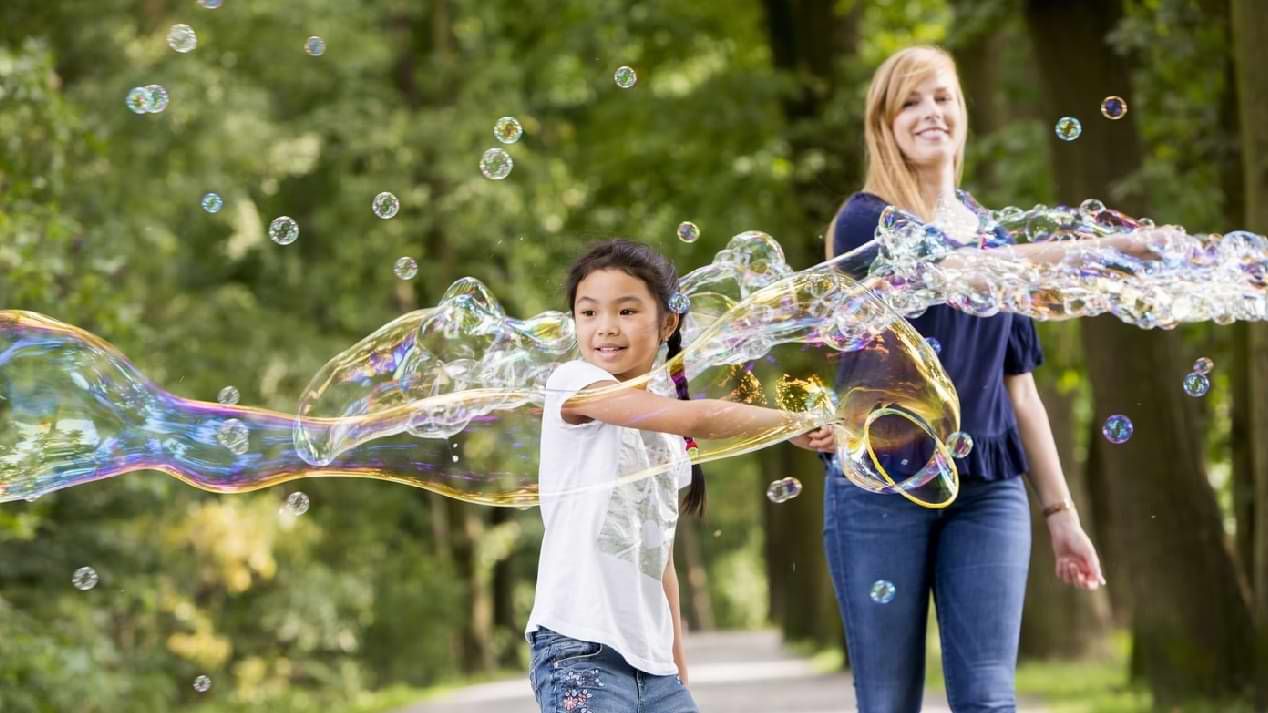 Eine junge, lächelnde Frau und ein Mädchen machen Seifenblasen.