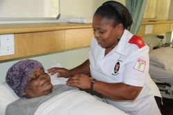 Nurse Nomusa Nxumalo caring for a patient at her bedside.