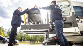 Malteser Mitarbeiter helfen einem Menschen im Rollstuhl ins Fahrzeug.