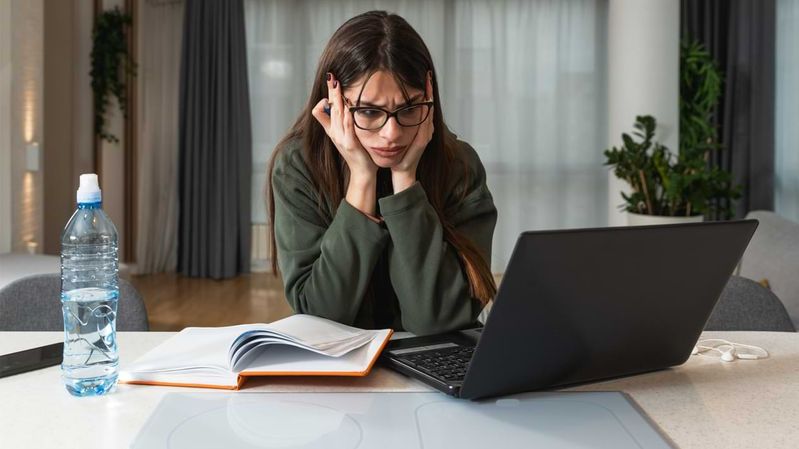 Eine junge Frau mit erschrockenem Geschichtsausdruck vor einem Laptop.