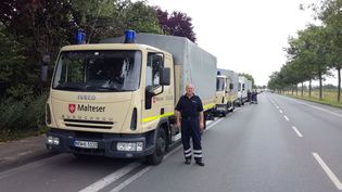 Malteser Mitarbeiter steht vor einer Fahrzeugkolonne mit Malteser Einsatzfahrzeugen