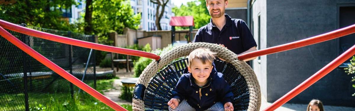 Ein Kind in einer Korbschaukel auf einem Spielplatz mit einem jungen Mann 