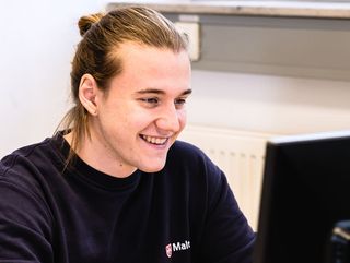 Junger Mann mit Malteser Pullover sitzt vor einem Laptop