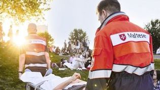 Zwei Sanitäter tragen eine verletzte Person über eine Wiese bei untergehenden Sonnen