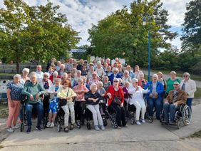 Viele Seniorinnen und Senioren haben sich für ein Gruppenbild im Freien zusammengefunden. In der ersten Reihe sind bewegeungseingeschränkte ältere Menschen im Rollstuhl positioniert.