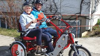 Ein Malteser Helfer fährt mit einer Seniorin Dreirad-Tandem.