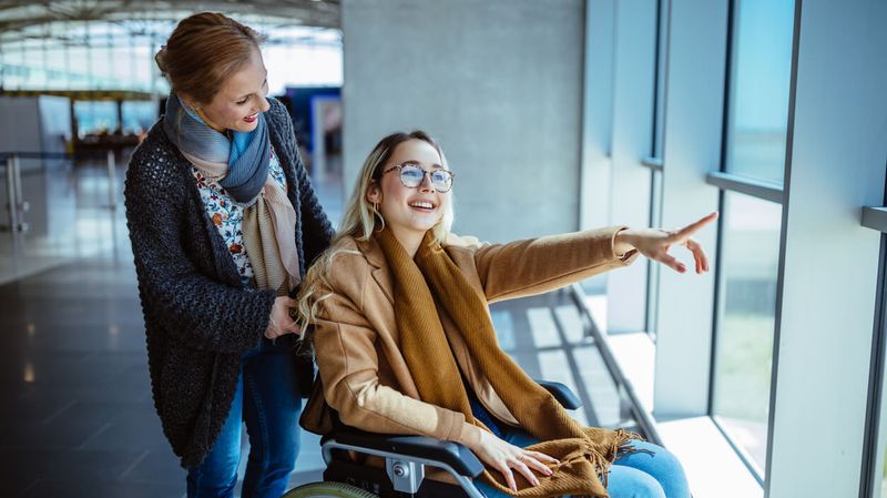Frau im Rollstuhl ud Pflegerin schauen aus einem Fenster