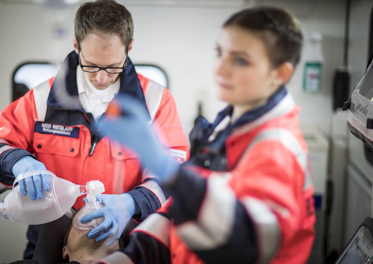 Zwei Notfallsanitäter legen einem Patienten im Krankenwagen eine Beatmungsmaske auf