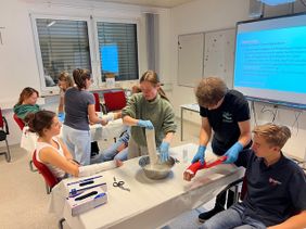 Auf dem Foto sind mehrere Personen zu erkennen, welche sich gegenseitig einen Gips anlegen.
